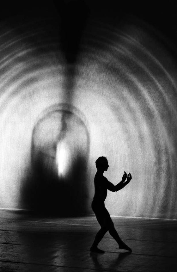 Die Silhouette eines Tänzers vor einem hellen, tunnelartigen Hintergrund.