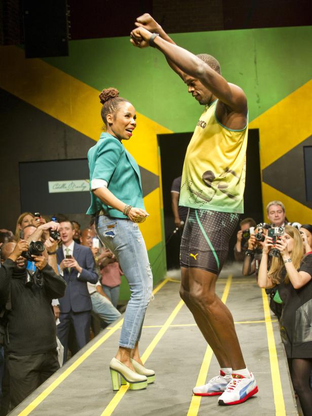 Usain Bolt und eine Frau posieren auf einem Laufsteg vor einer Wand in den jamaikanischen Nationalfarben.
