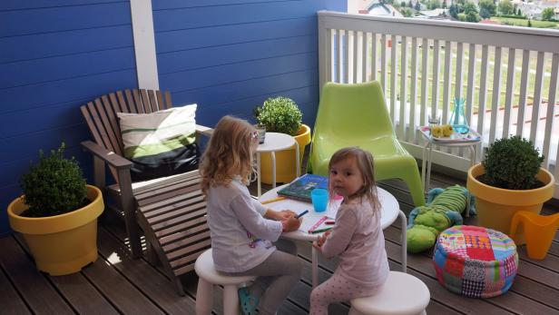 Zwei kleine Mädchen sitzen an einem Tisch auf einer Terrasse und malen.