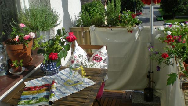 Ein sonniger Balkon mit Blumen, Kräutern und einem Tisch mit Dekorationen.