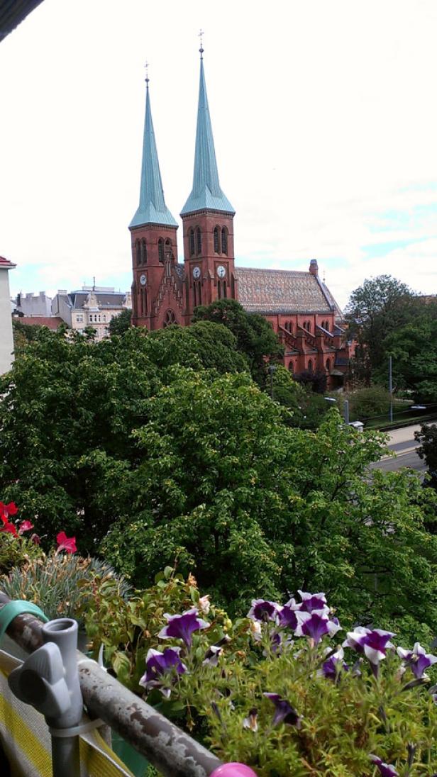 Blick von einem Balkon auf eine rote Backsteinkirche mit zwei spitzen Türmen.