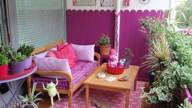 Ein gemütlicher Balkon mit lila Akzenten, Pflanzen und einer kleinen Sitzecke.