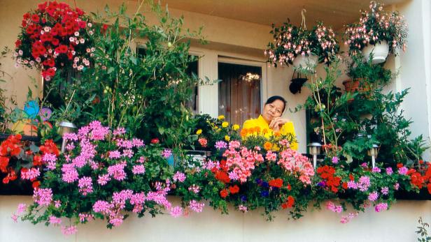 Eine Frau lächelt hinter einem Balkonkasten voller Blumen.