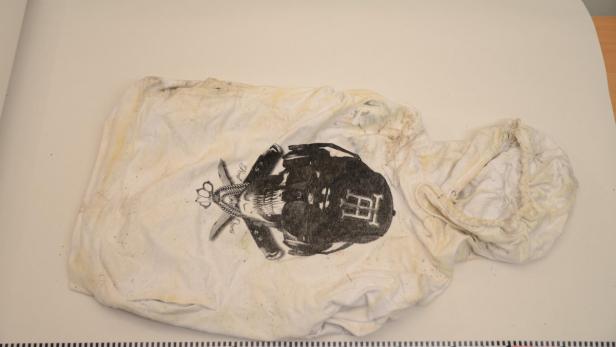 Ein verschmutzter, weißer Kapuzenpullover mit einem Totenkopf-Motiv liegt auf einem Tisch.