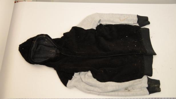 Eine schwarze und graue Kapuzenjacke liegt auf einem weißen Untergrund.