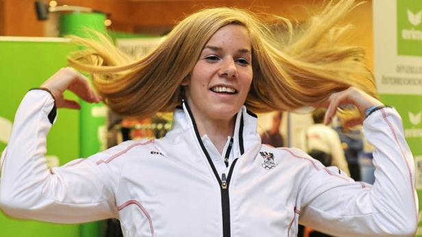 Eine blonde Frau in einer weißen Jacke wirft ihre Haare in die Luft.