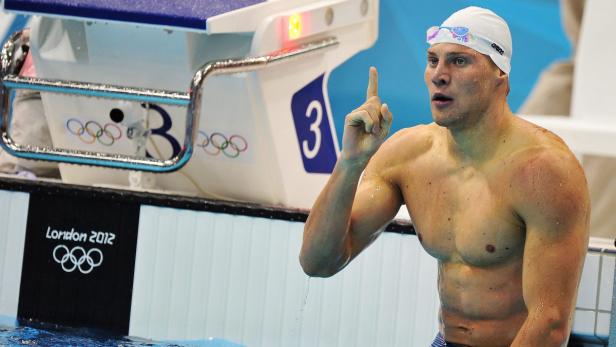 Ein Schwimmer am Beckenrand der Olympischen Spiele 2012 in London zeigt mit dem Finger nach oben.