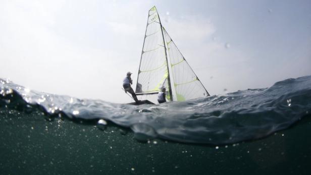 Zwei Segler auf einem Segelboot, gesehen aus der Wasserperspektive.