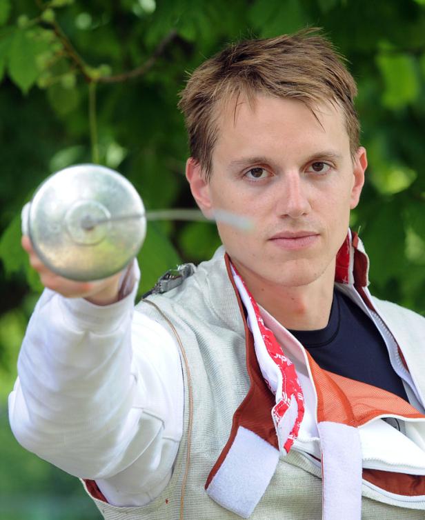 Ein junger Mann in Fechtausrüstung hält einen Degen in der Hand.
