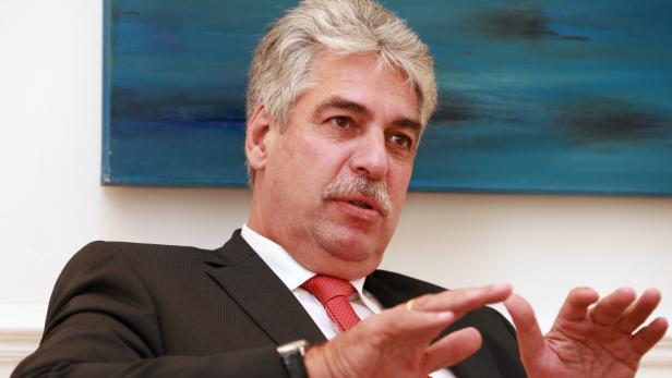 Ein Mann im Anzug gestikuliert vor einem blauen Gemälde.