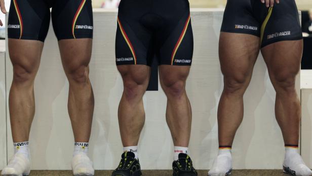 Die muskulösen Beine von drei Radrennfahrern in Radsportbekleidung stehen nebeneinander.