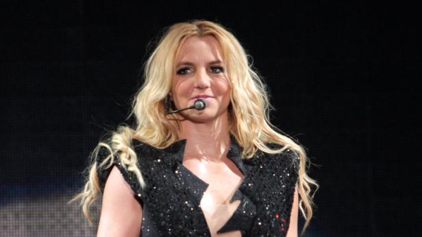 Britney Spears mit blonden, gewellten Haaren und einem schwarzen, glitzernden Oberteil singt.