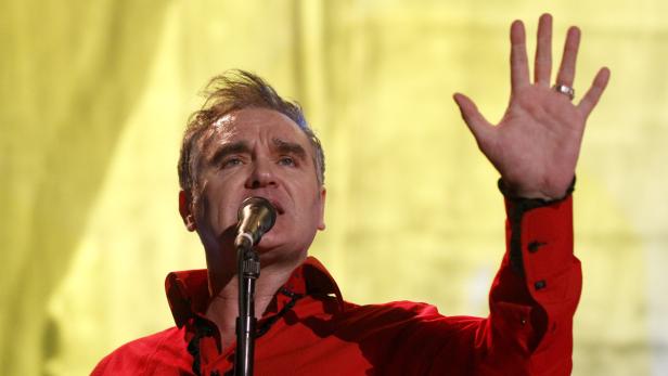 Morrissey singt in einem roten Hemd und hebt seine Hand.