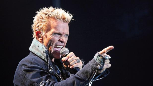 Billy Idol singt mit einem Mikrofon in der Hand und zeigt mit dem Finger.