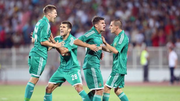 Vier Fußballspieler in grünen Trikots jubeln auf dem Spielfeld.