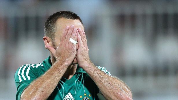 Ein Fußballspieler im grünen Trikot verdeckt sein Gesicht mit den Händen.