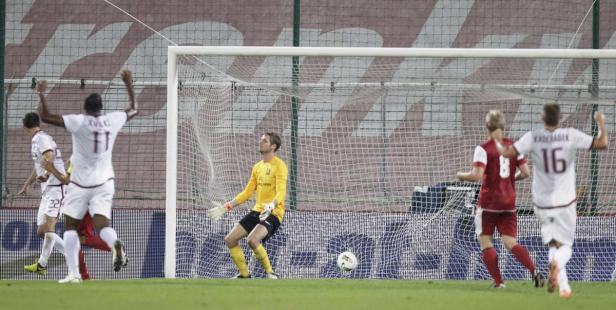 Fußballspieler jubeln vor dem Tor, während der Torwart den Ball beobachtet.