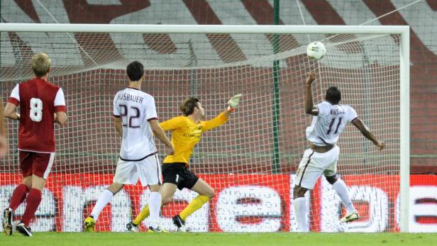 Ein Fußballspieler köpft den Ball vor dem Tor, während der Torwart versucht, ihn abzuwehren.