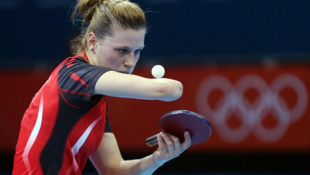 Eine Frau spielt Tischtennis vor dem Hintergrund der olympischen Ringe.