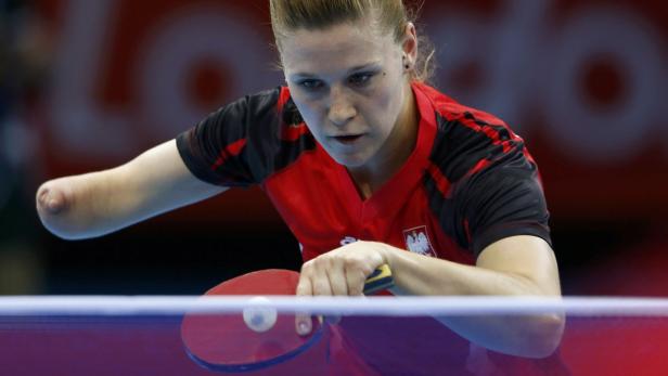 Eine behinderte Tischtennisspielerin im rot-weißen Trikot bei einem Aufschlag.