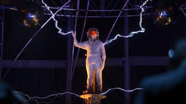 Eine Person in einem Kettenhemdanzug steht unter Stromblitzen.