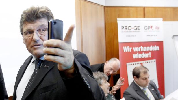 Ein Mann im Anzug hält ein Smartphone in die Höhe.