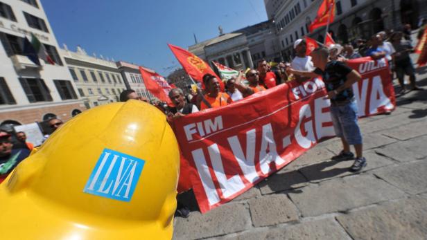 Eine Demonstration mit roter Fahne und einem gelben Bauhelm mit dem ILVA-Logo.