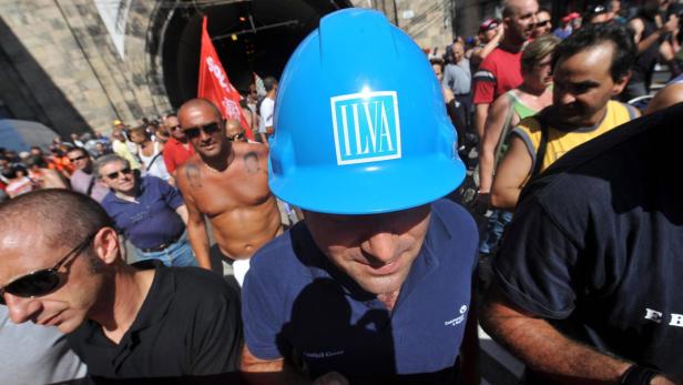 Ein Mann mit blauem ILVA-Helm steht in einer Menschenmenge.