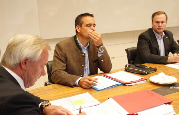 Drei Männer sitzen an einem Tisch mit Dokumenten während einer Besprechung.