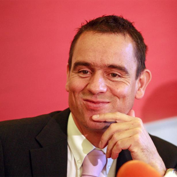 Ein Mann im Anzug lächelt und hält seine Hand ans Kinn.