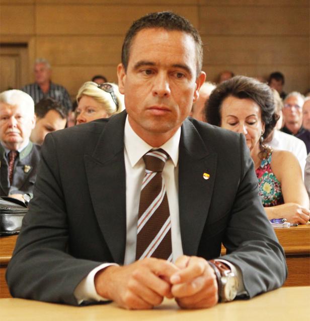 Ein Mann im Anzug sitzt mit verschränkten Händen an einem Tisch.