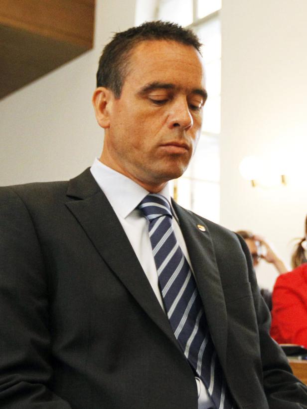 Ein Mann im Anzug mit gestreifter Krawatte blickt nach unten.