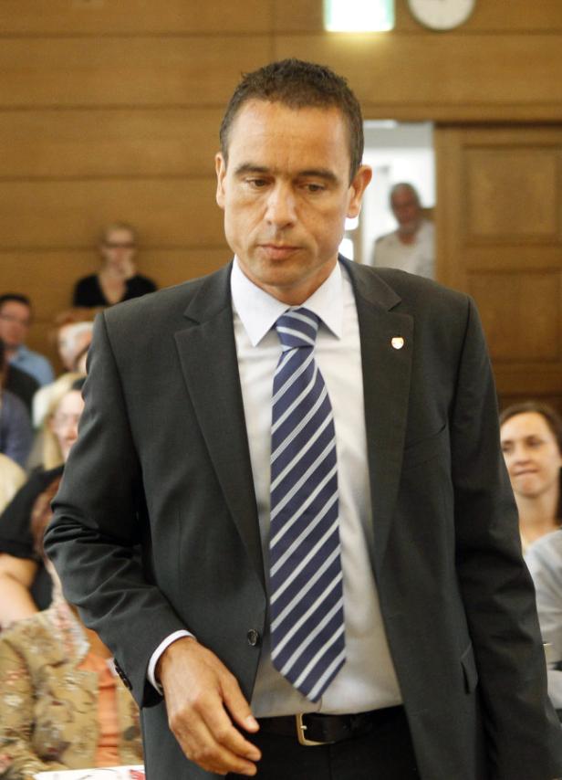 Ein Mann in Anzug und Krawatte steht vor einer Gruppe von Menschen.