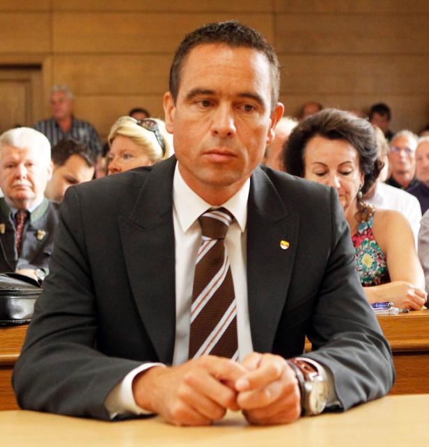 Ein Mann im Anzug sitzt mit verschränkten Händen an einem Tisch.