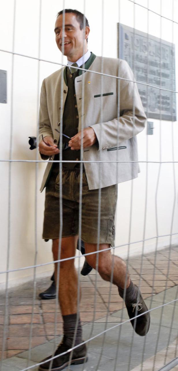 Ein Mann in Tracht geht hinter einem Zaun entlang.