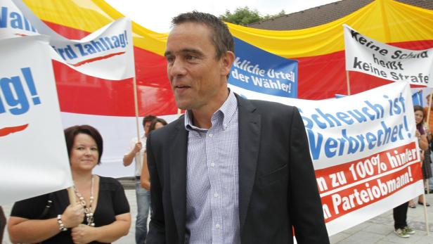 Ein Mann in Anzug steht inmitten einer Demonstration mit Protestschildern.