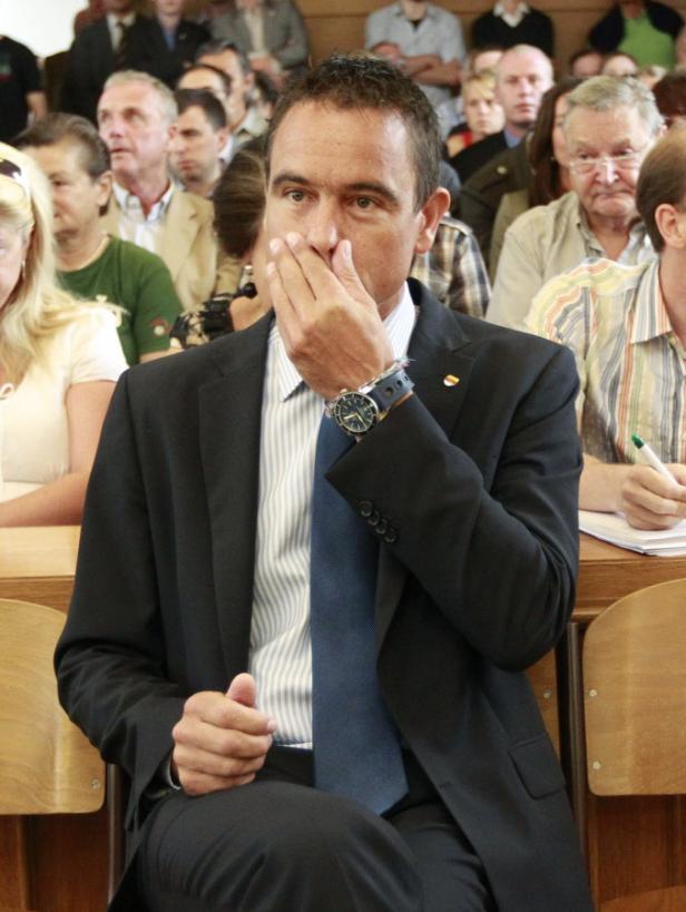 Ein Mann im Anzug sitzt im Publikum und hält seine Hand vor den Mund.