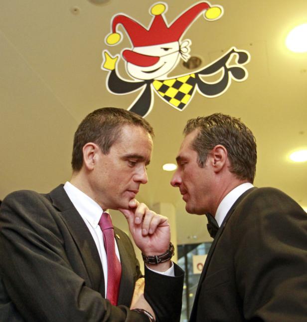 Zwei Männer in Anzügen unterhalten sich unter einem Karneval-Deckenbild.