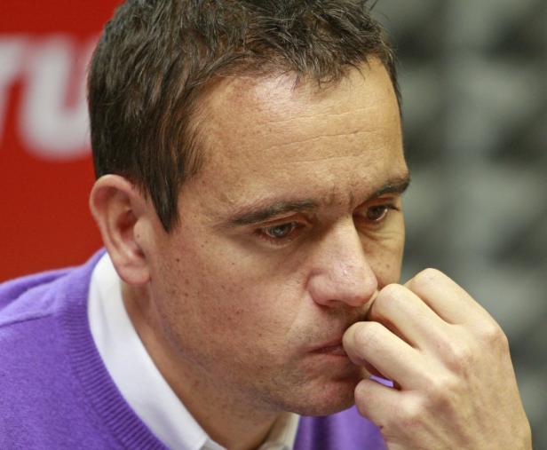 Ein Mann im lila Pullover kaut nachdenklich auf seinen Fingern.