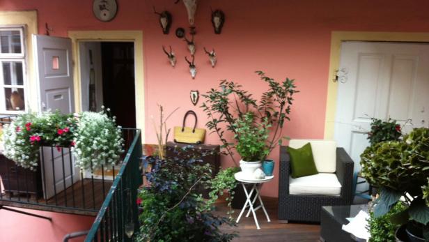 Ein gemütlicher Balkon mit Pflanzen, Möbeln und Dekorationen an einer rosa Wand.