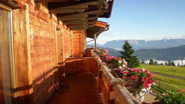 Blick vom Balkon eines Holzhauses auf eine grüne Landschaft mit Bergen im Hintergrund.