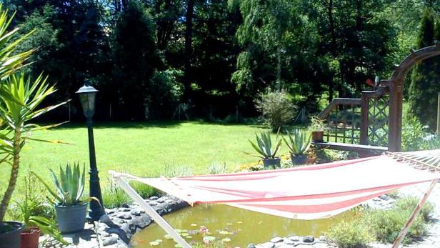 Eine rot-weiß gestreifte Hängematte hängt über einem kleinen Teich in einem Garten.