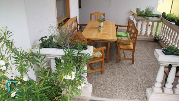Ein Holztisch und Stühle stehen auf einer Terrasse mit Pflanzen.
