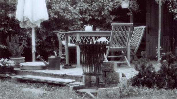 Ein Gartentisch mit Teekanne und Tasse auf einer hölzernen Terrasse.