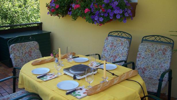 Ein gedeckter Tisch mit Baguette, Tellern und Gläsern auf einer Terrasse.