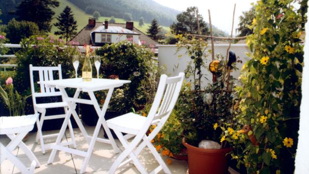 Auf einem Balkon mit üppiger Bepflanzung stehen ein Tisch und Stühle bereit für ein entspanntes Beisammensein.