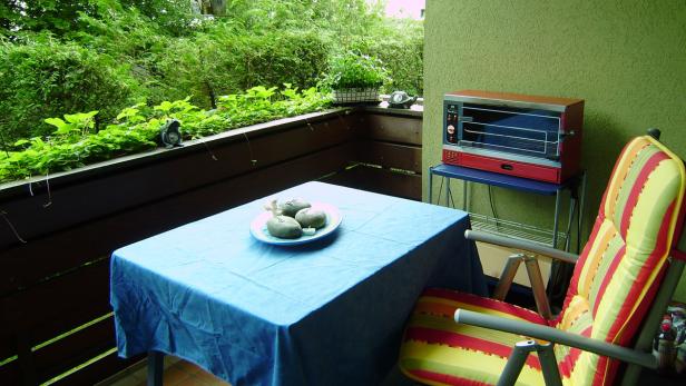 Ein gedeckter Tisch und ein Grill auf einem begrünten Balkon.