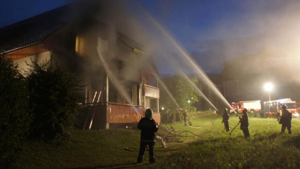 Feuerwehrleute löschen ein brennendes Haus mit Wasserwerfern.