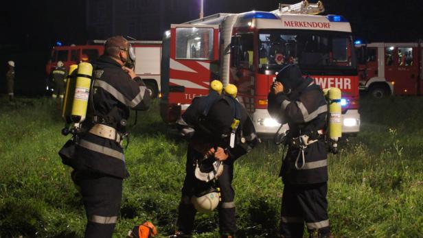 Drei Feuerwehrleute in voller Montur bereiten sich auf einen Einsatz vor einem Feuerwehrauto vor.