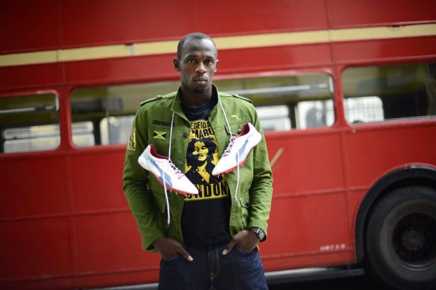 Usain Bolt posiert mit Spikes vor einem roten Doppeldeckerbus.